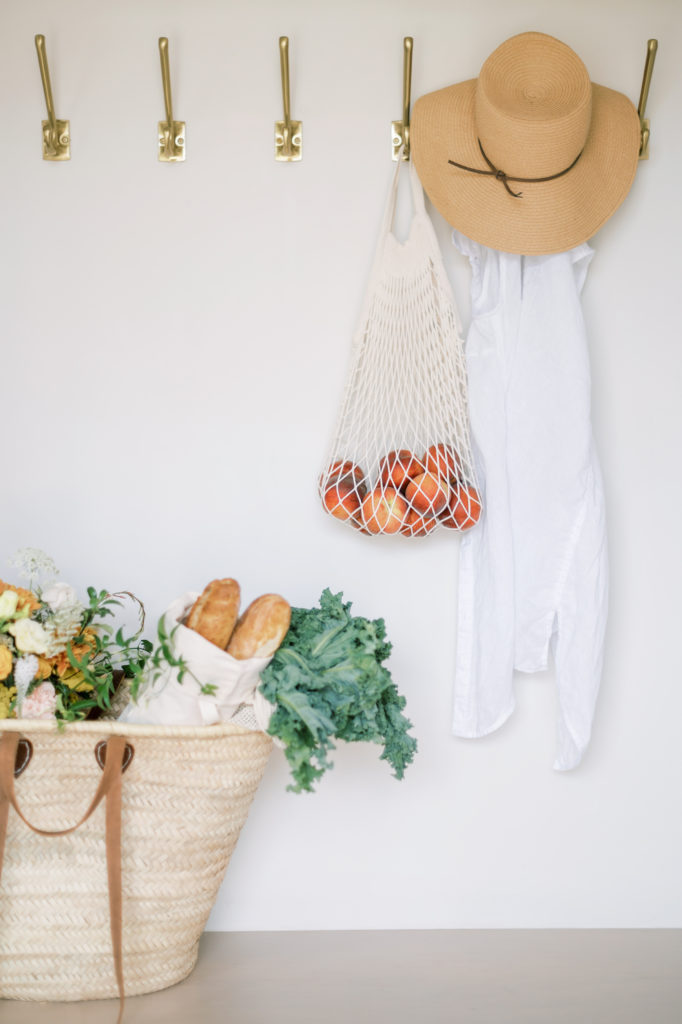 Reusable bag filled with groceries next to a sweater and hat.