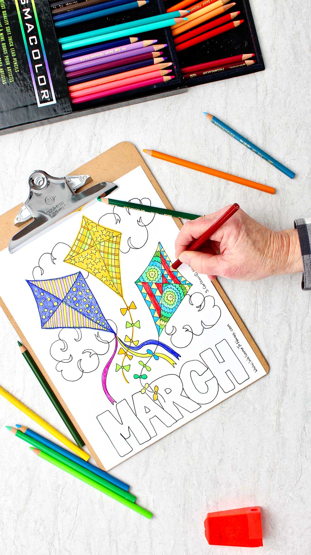 Hand coloring a pattern on the kite on the right side with a red colored pencil. All three kites are colored in.