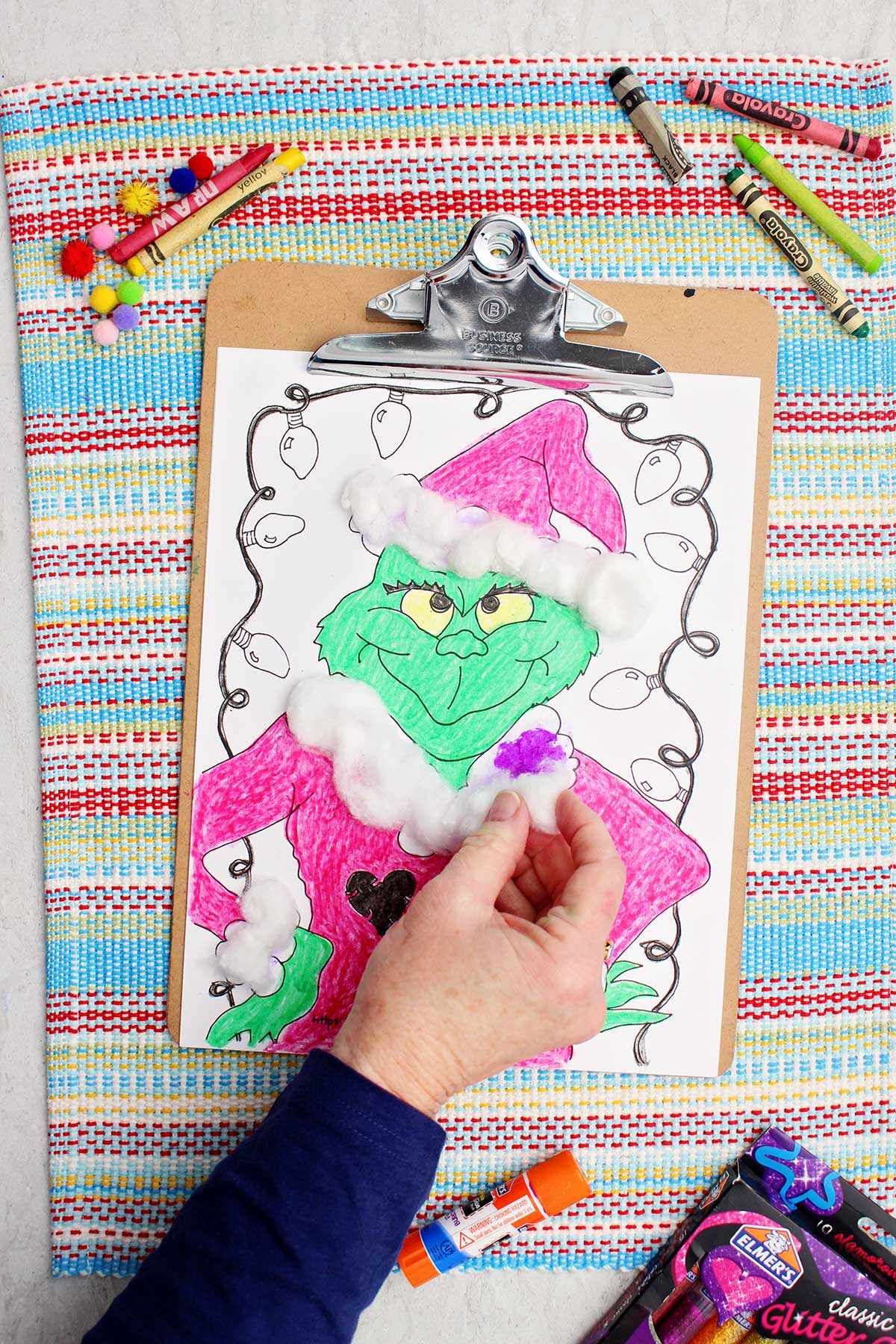 Person gluing cotton balls on the Grinch's Santa coat.
