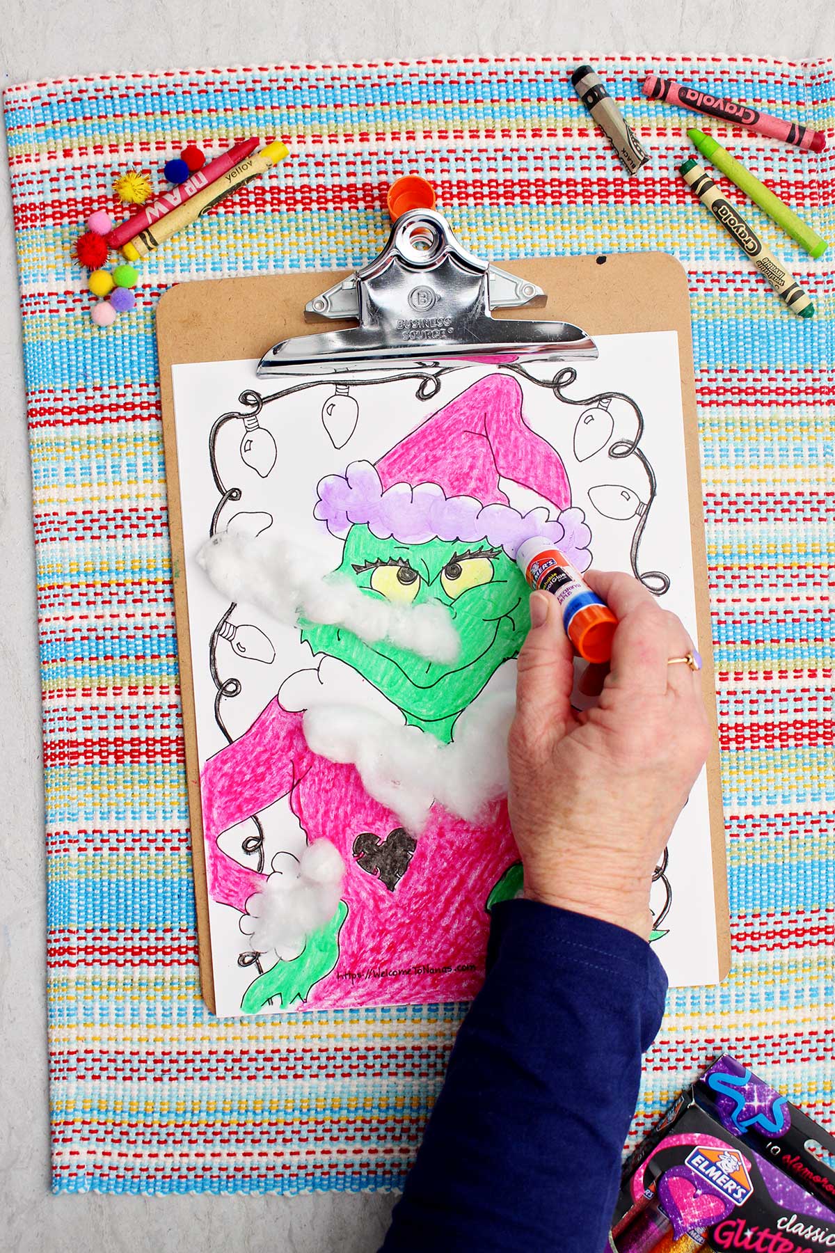 Person putting purple glue stick on Santa hat accent for attaching cotton balls.