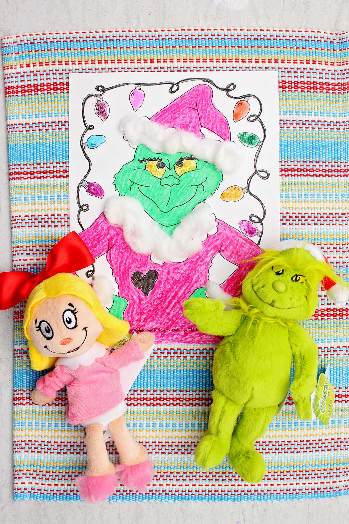 Completed Grinch coloring page with two Grinch stuffed animals near by.