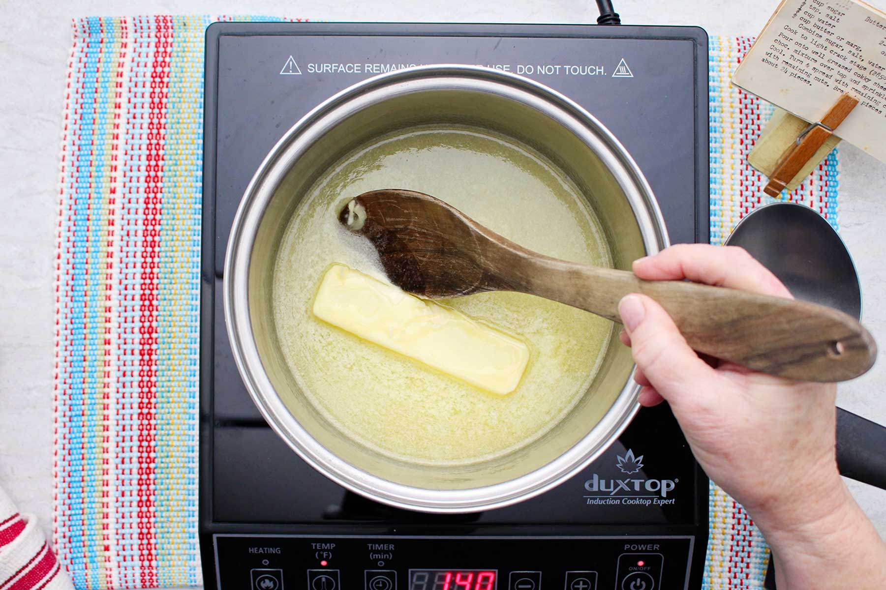 A person melting butter in a saucepan.