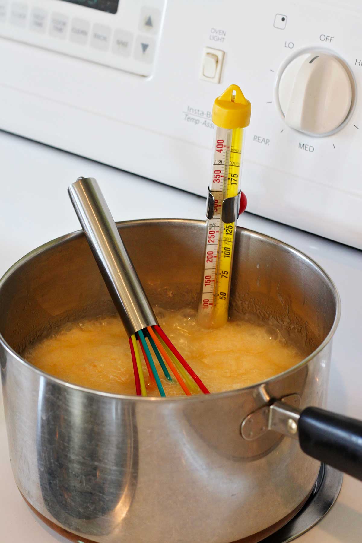 Fudge mixture simmering on the stove with a candy thermometer reading the temperature.