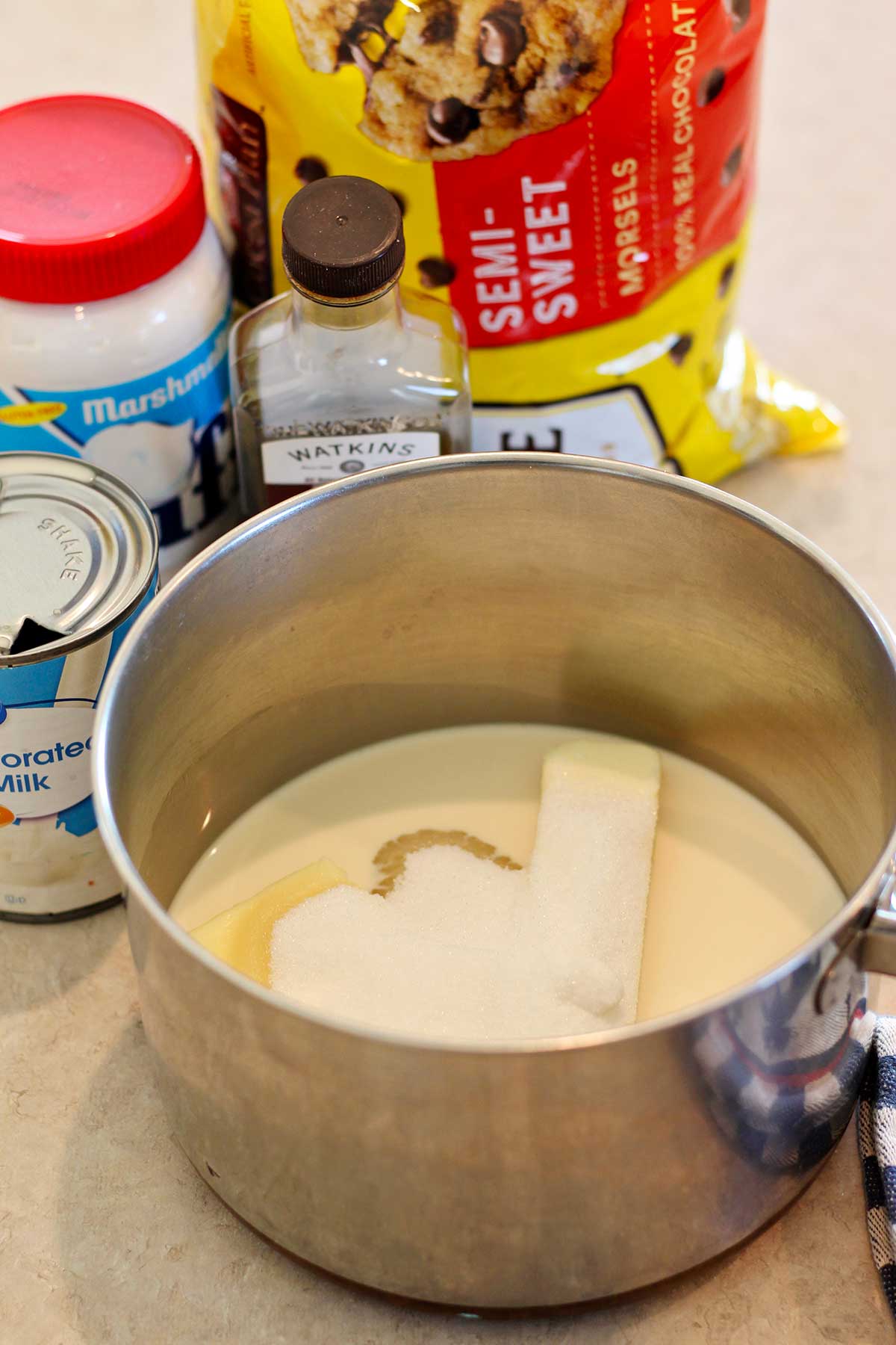 A saucepan full of evaporated milk, butter and sugar with other ingredients in the background.