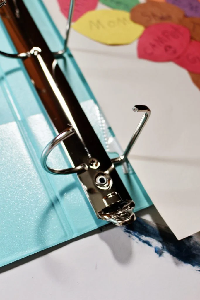 A binder opened to add pages, a child's piece of artwork in the background.
