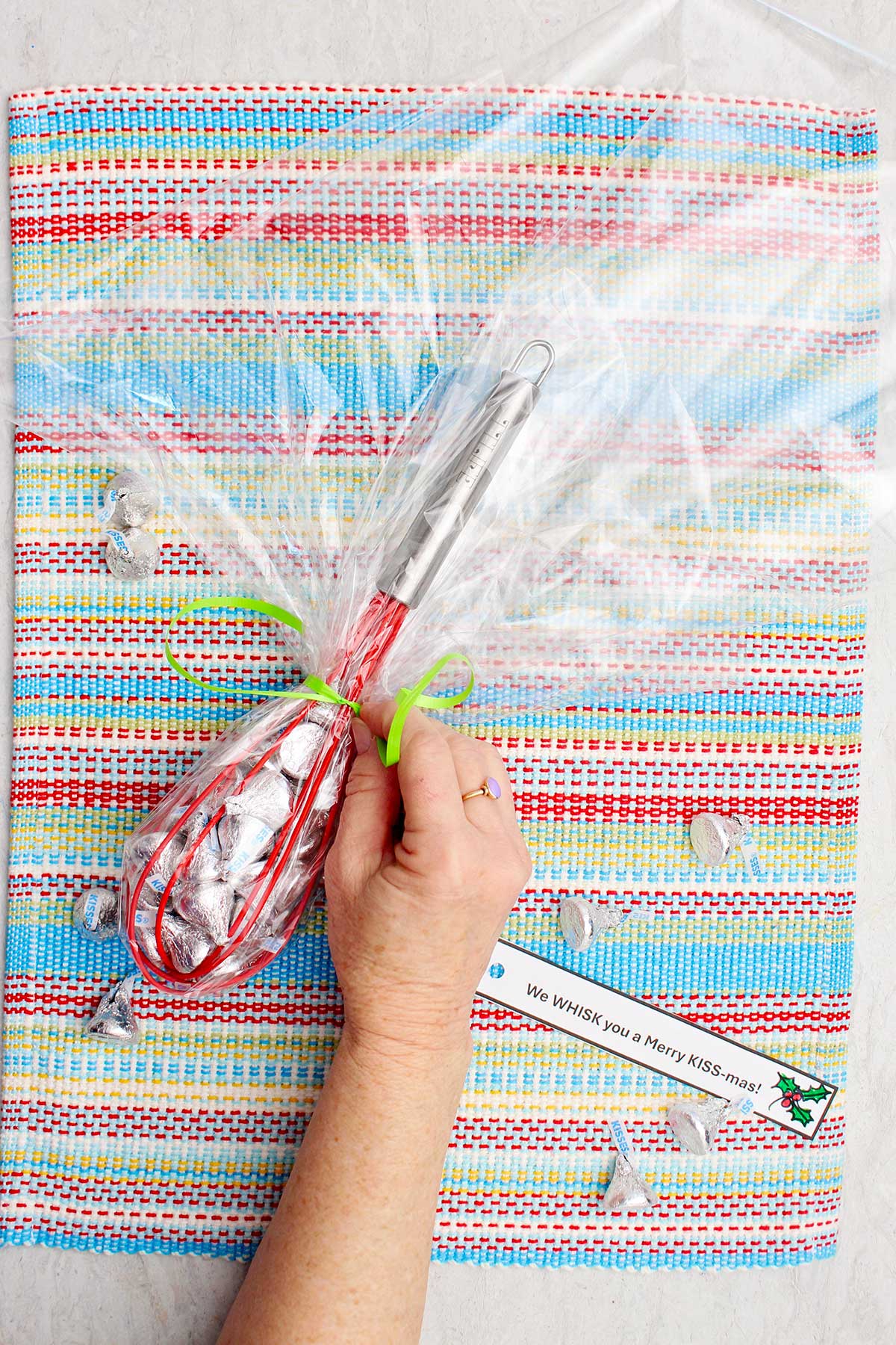 Person securing a green ribbon around the wrapped candy whisk.