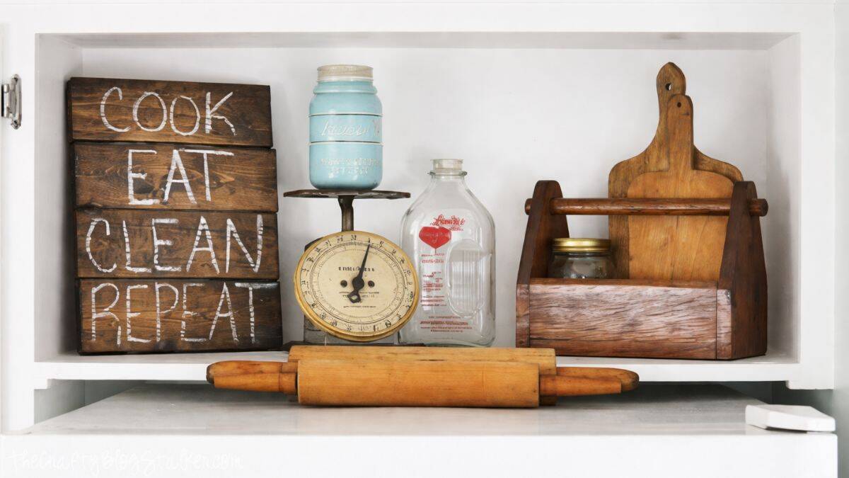Farmhouse kitchen shelf decor with wooden sign reading Cook Eat Clean Repeat, vintage scale, milk bottle, mason jar, cutting boards, and rolling pin.