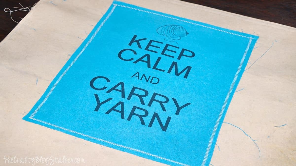 Blue Keep Calm and Carry Yarn fabric panel stitched onto canvas tote bag fabric during sewing project.