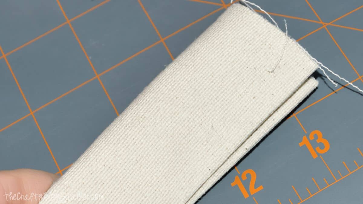 Folded canvas strap with stitched edges shown on a cutting mat during assembly of a handmade tote bag strap.
