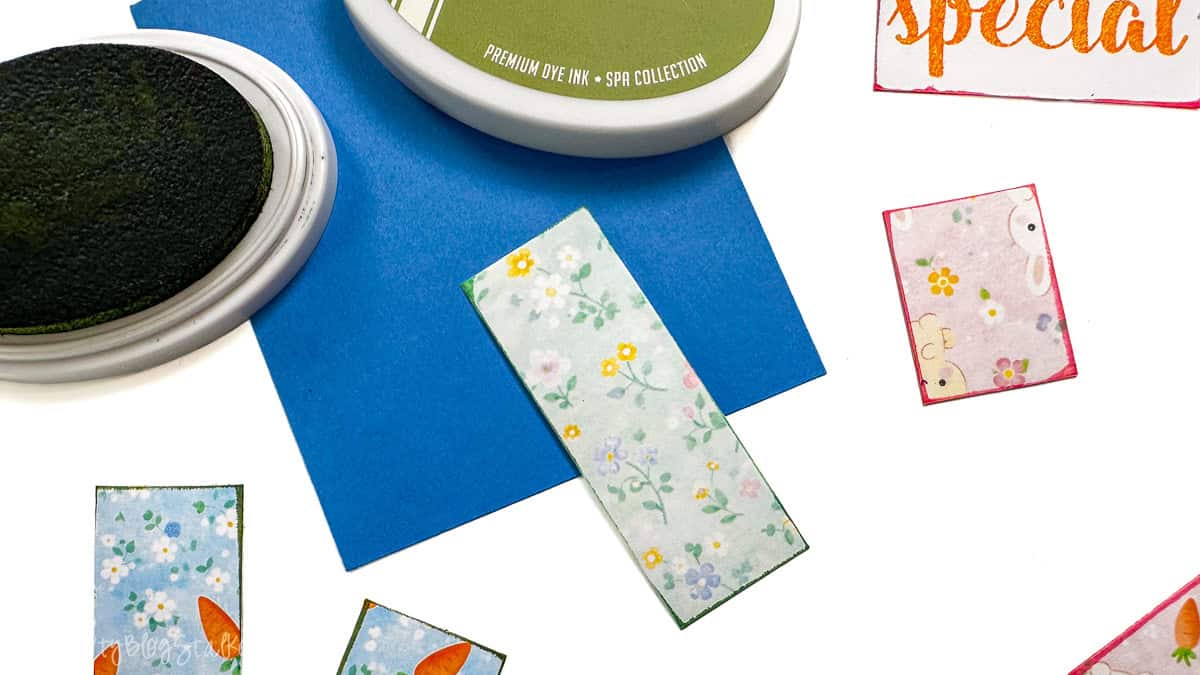 Ink pads and small patterned paper pieces on a table, showing edges being inked before assembling a handmade card.