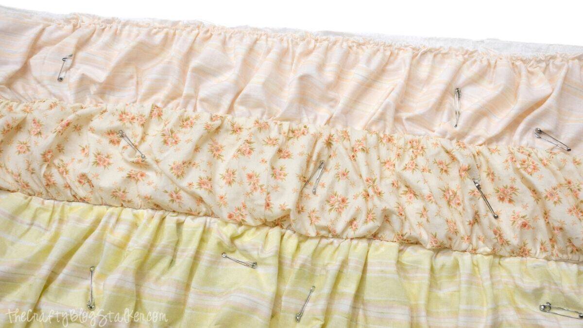 6- pin layers together Ruffled quilt top layers pinned together with safety pins, showing gathered fabric strips secured in place before sewing.