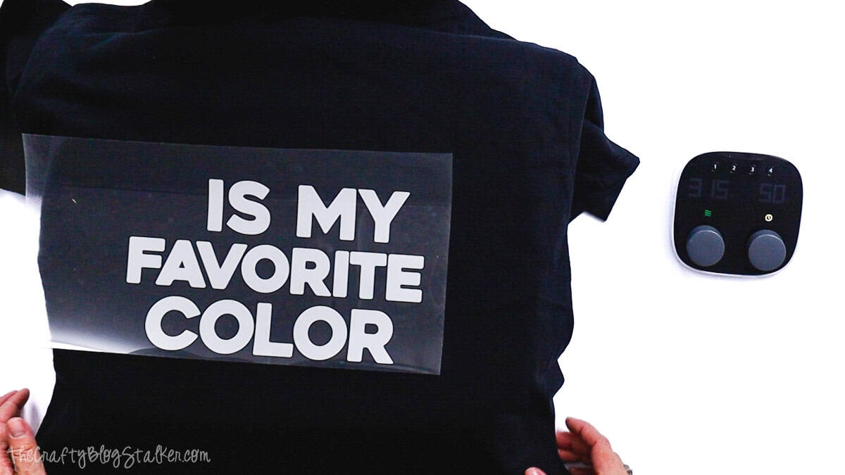 Iron-on vinyl text placed on the back of a T-shirt and covered with a carrier sheet, ready to be pressed with a heat press.