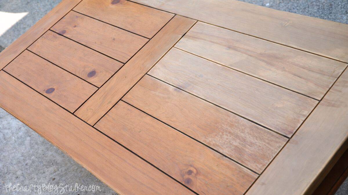 Close-up of a wooden coffee table top with a plank-style design, showing the surface being sanded to prep the wood for refinishing.