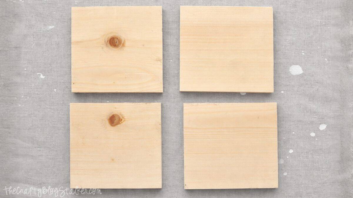 Four unfinished square wooden boards arranged in a grid on a fabric-covered work surface, ready for a DIY craft or home decor project.