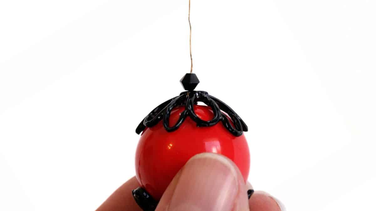 Close-up of a beaded spider body on headpin, held between fingers while assembling a handmade spider craft.