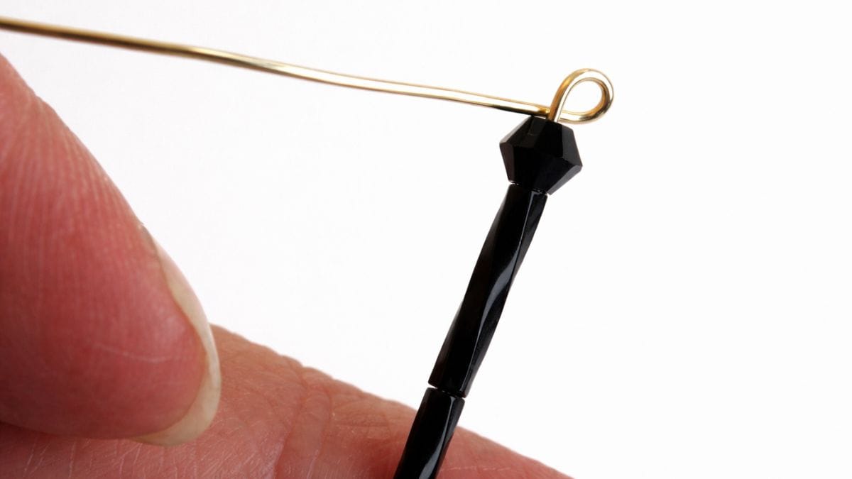 Close-up of a beaded wire leg with a small loop formed at the end, held between fingers during assembly of a spider craft.