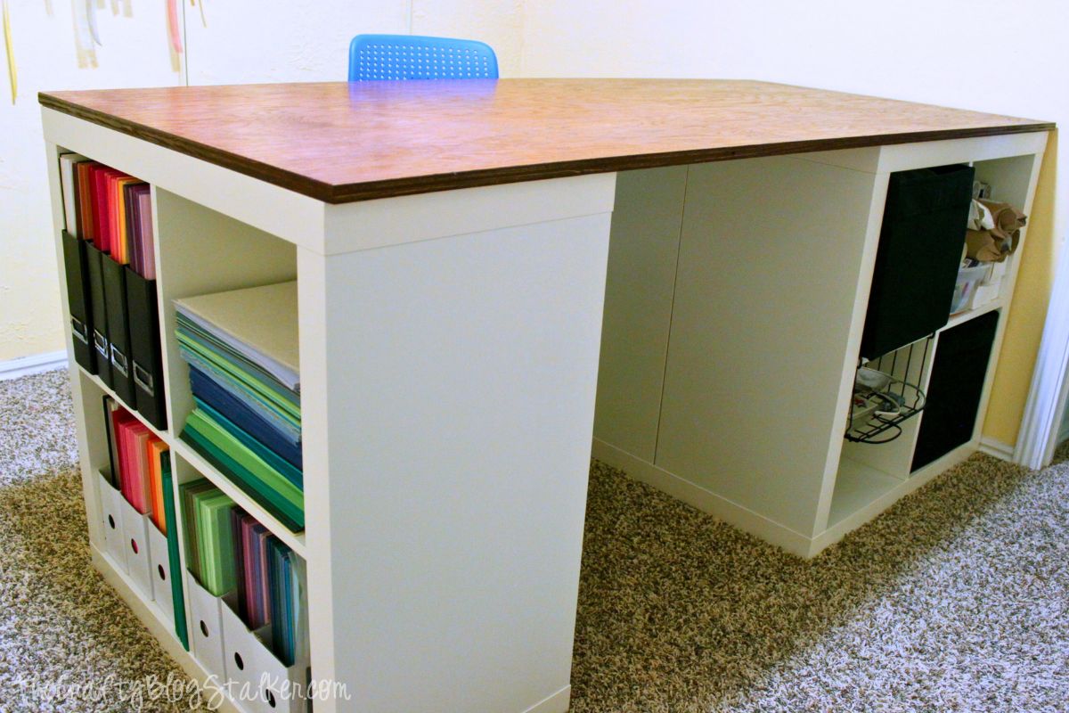 A DIY crafting table made from white cube storage units with a stained wooden top, providing ample workspace and organized storage for craft supplies and materials.