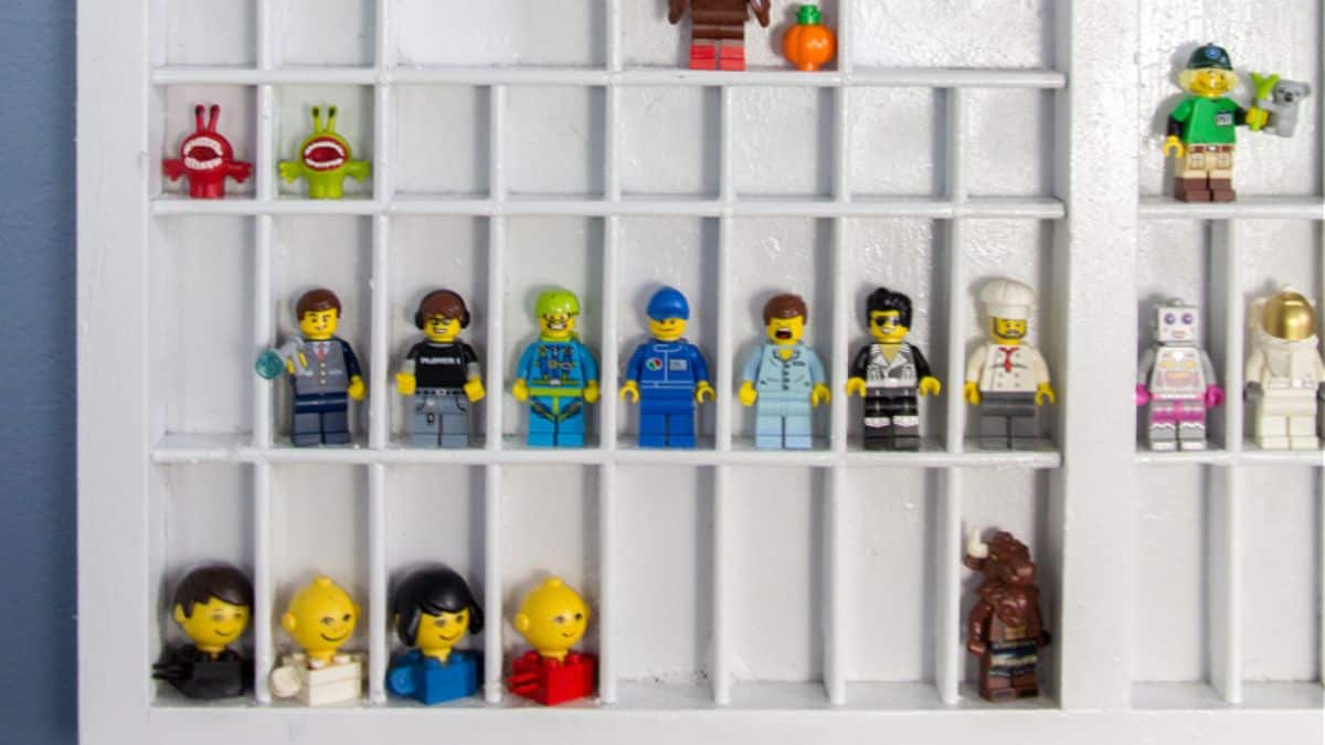 Wall-mounted display shelf with small cubbies holding LEGO minifigures, arranged in rows to showcase a collection of characters and accessories.
