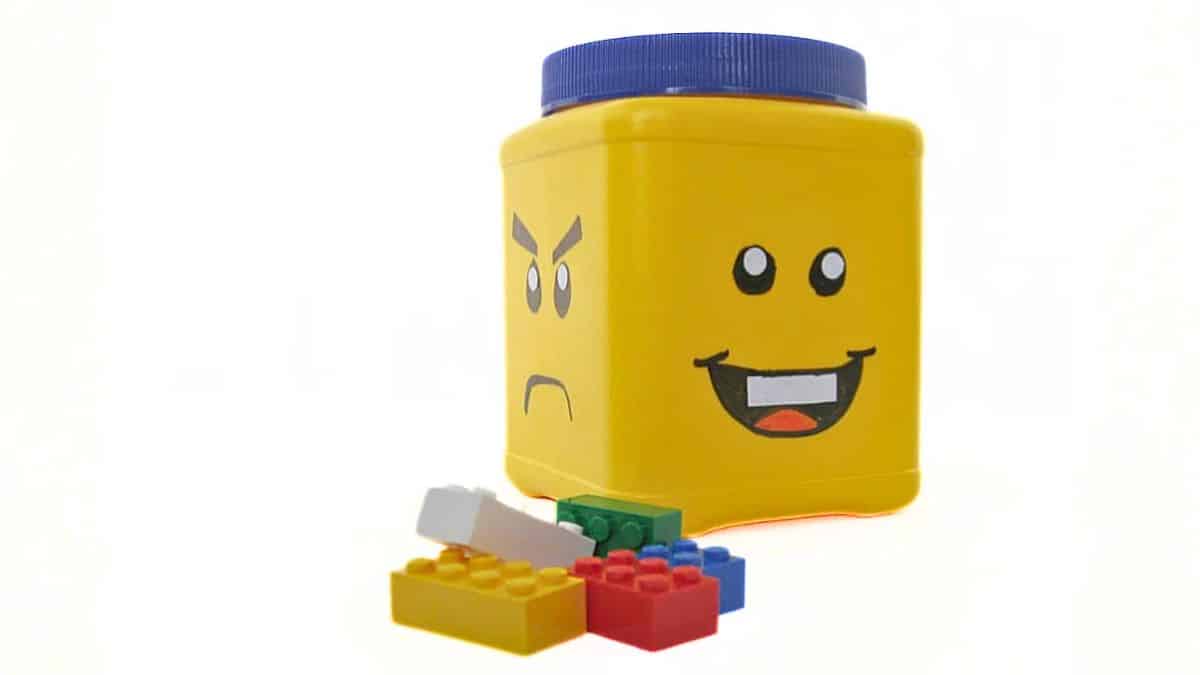 Repurposed plastic container decorated like a LEGO minifigure head, with different facial expressions and LEGO bricks scattered in front.