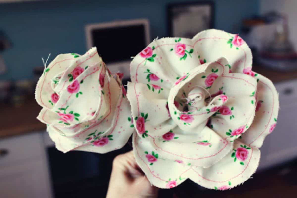 Hand holding two handmade fabric roses made from patterned cotton, showing layered petals and stitched edges as a DIY fabric flower craft.