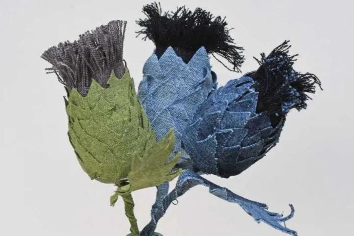 Three handmade fabric thistle flowers with textured leaves and fringe-style tops, arranged together against a plain background.