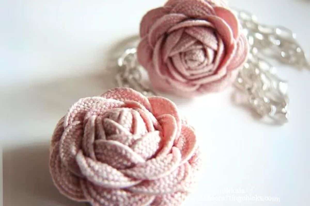 Two handmade rick rack rosette flowers attached to chain jewelry, shown close up as fabric flower embellishments on a white surface.