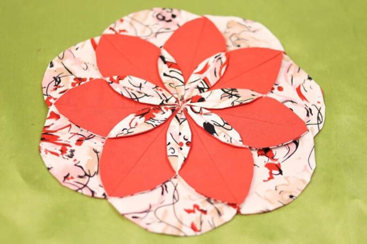 Layered fabric flower table topper with petal-shaped pieces arranged in a circular design, shown flat on a solid background.