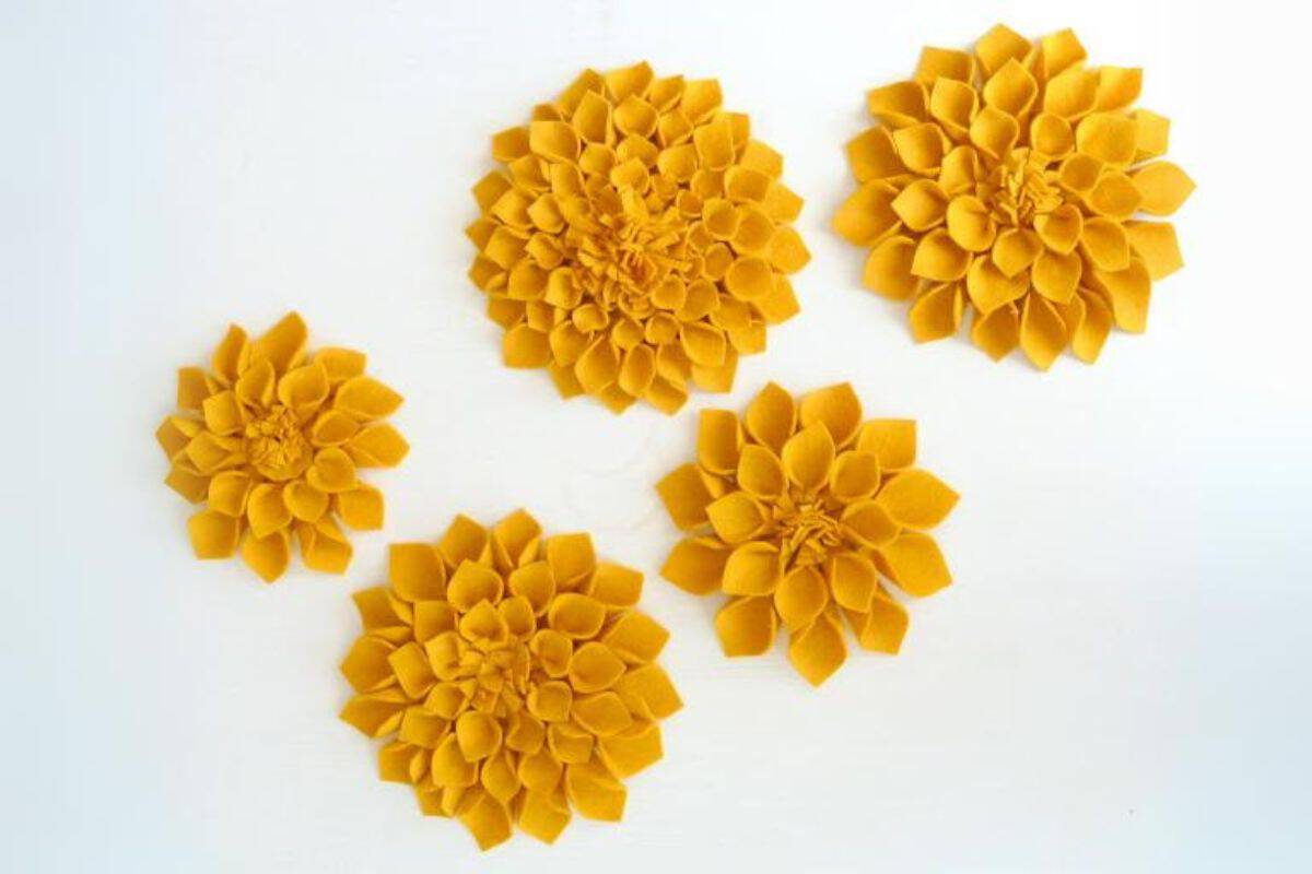 Five handmade felt flowers arranged on a white background, showing layered petal shapes and varying sizes in a flat lay arrangement.