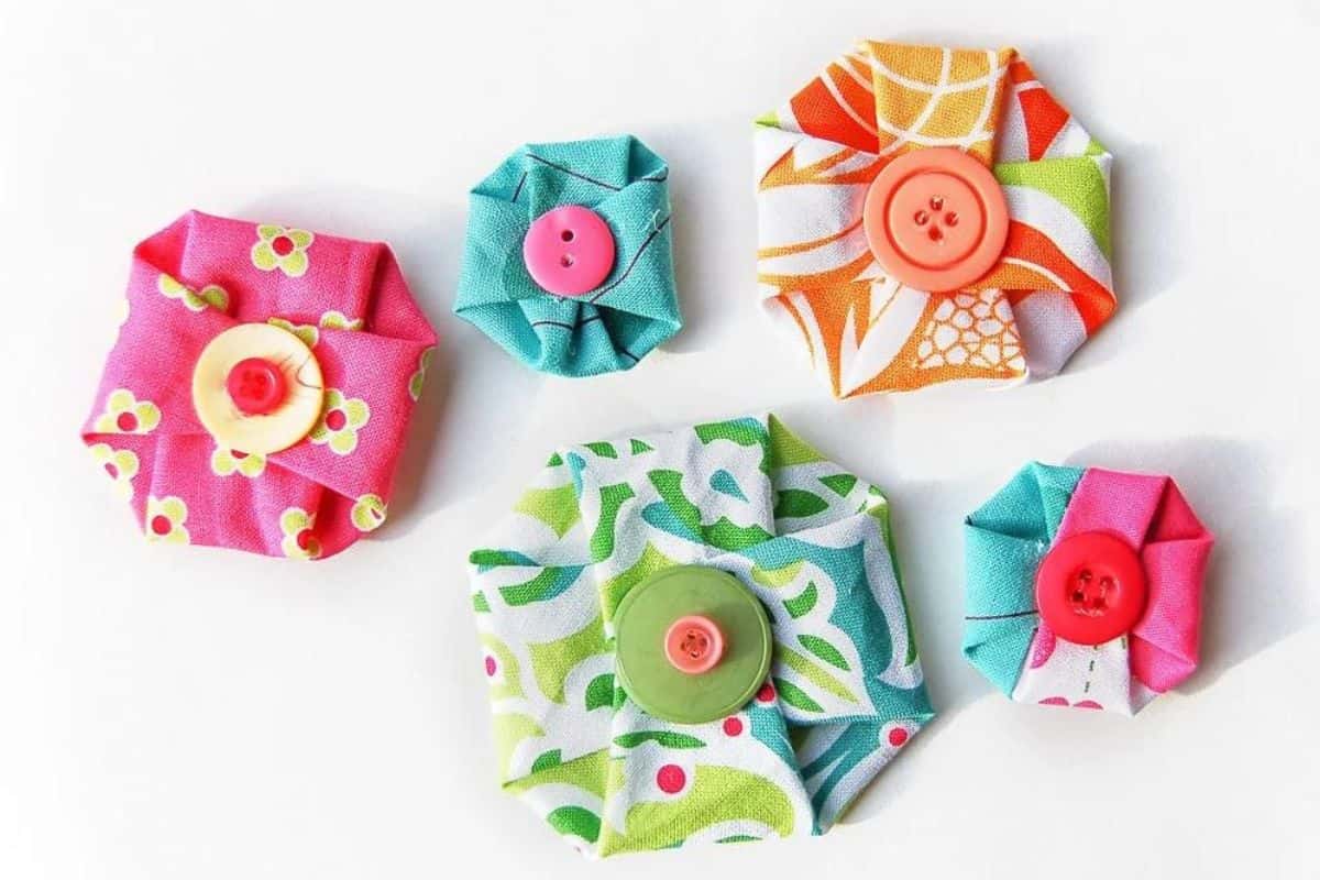 Assorted handmade no-sew fabric flowers in different sizes and patterns, each folded into a rosette shape and finished with a button center.
