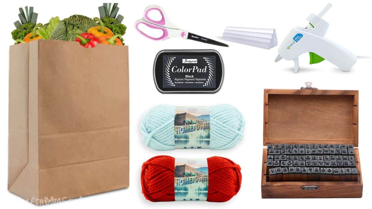 Flat lay of gift wrapping supplies including a paper grocery bag, yarn skeins, ink pad, glue gun with glue sticks, and a wooden box of letter stamps.
