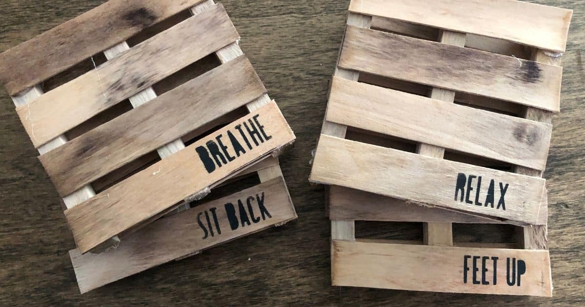Two handmade mini pallet wood coasters with rustic slats, featuring stamped words like breathe, sit back, relax, and feet up on a wood surface.