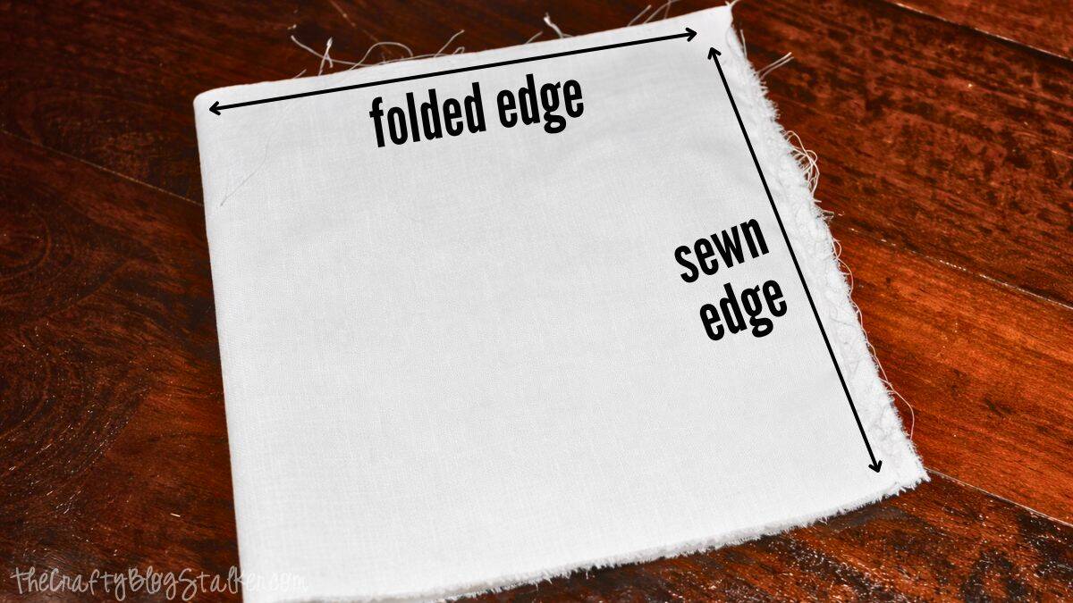 Fabric square for a stocking cuff with labeled folded edge and sewn edge, shown flat on a wooden surface as part of a step-by-step sewing tutorial.