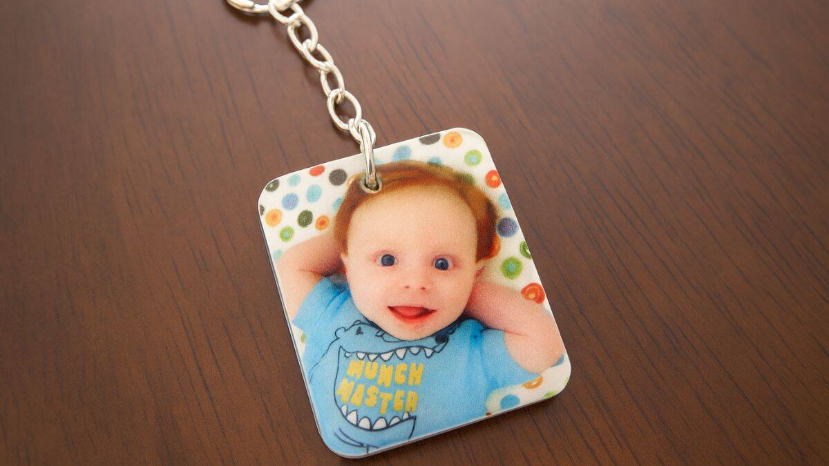 Personalized photo keychain featuring a printed picture of a smiling baby on a rectangular charm attached to a metal keychain.