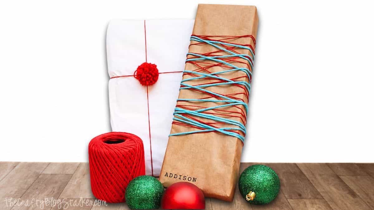 Wrapped holiday gifts decorated with yarn and twine, featuring kraft paper and white paper packages displayed with spools of yarn and ornaments.