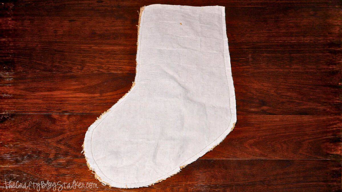 Fabric stocking shape with a sewn lining, showing stitched edges and seams laid flat on a wooden work surface during a DIY stocking project.