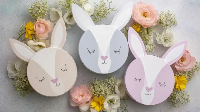 Three Easter bunny gift boxes lie next to spring blossoms