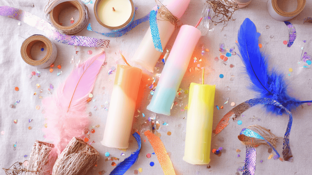 Candles using the di-dye technique lie between feathers and confetti on a base made of beige fabric.