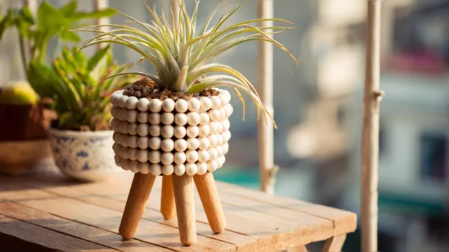 A flower pot made of wooden balls with standing feet stands on a balcony table