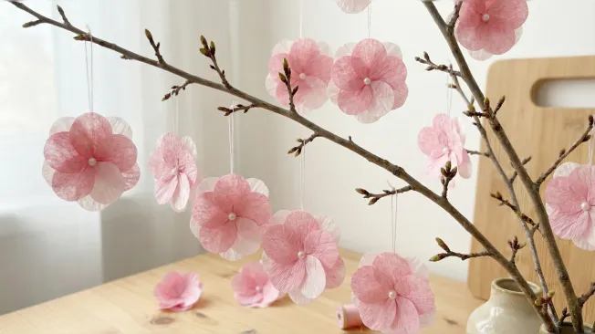 Pink cherry blossoms made from napkins hang on spring branches.