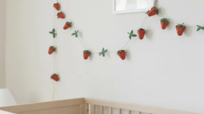 An egg carton strawberry garland hangs over a baby bed.