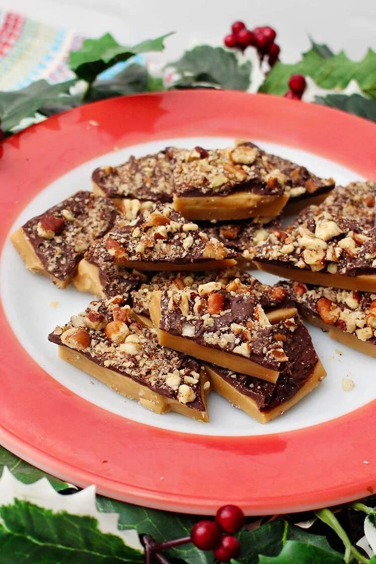 Red rimmed plate of English toffee with festive ivy surrounding it.