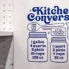 Blue kitchen conversion chart decal on a wall near a stove, showing tablespoon, cup, pint, quart, and gallon measurements with illustrated jars and measuring tools.