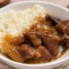 Bowl of slow cooker beef tips in rich gravy served over fluffy white rice on a rustic table setting.